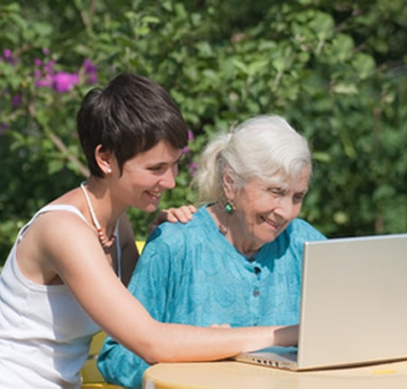 Oudere persoon die samen met een zorgverlener informatie opzoekt op internet in een woonzorgcentrum om het geheugen en de cognitieve functies te stimuleren.
